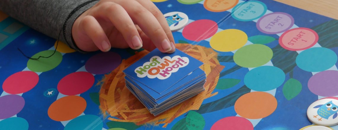 child's hand reaches for a card while playing a cooperative board game