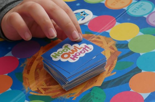 child's hand reaches for a card while playing a cooperative board game