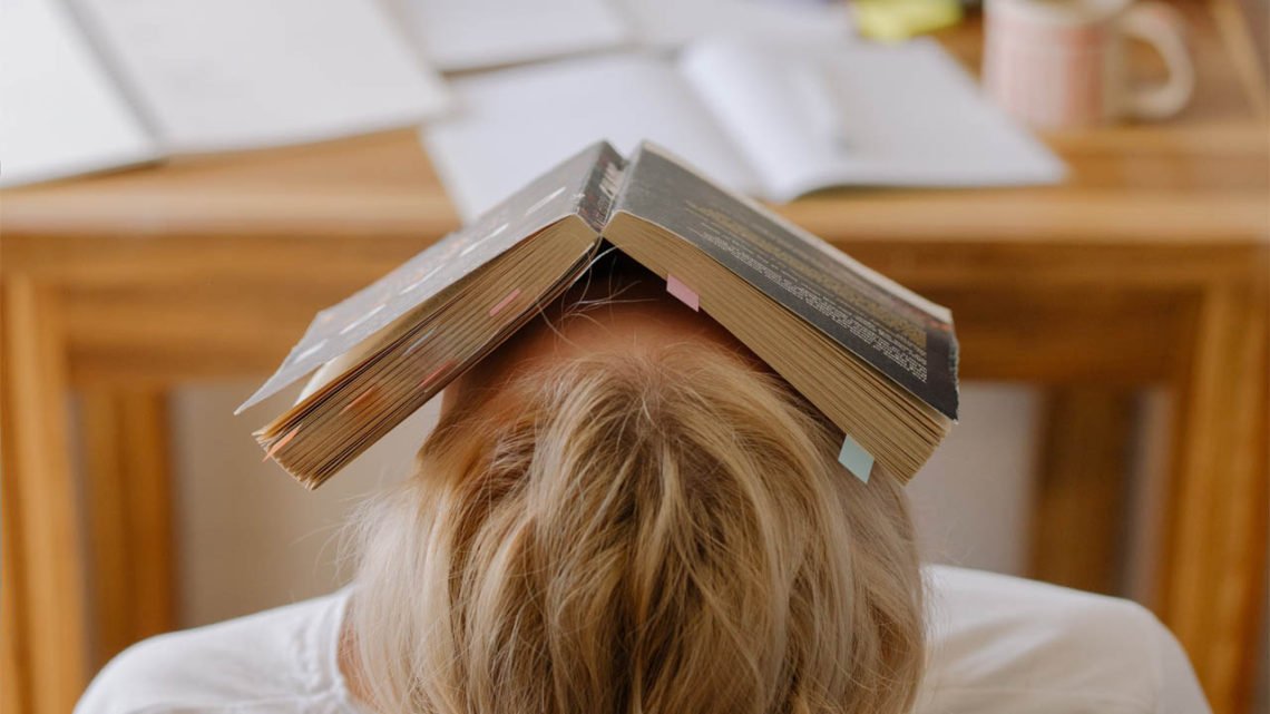 child sits at a desk with an open book over their face