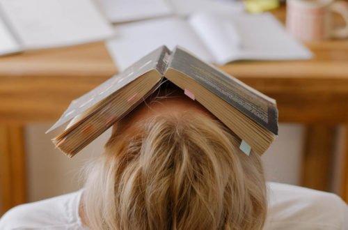 child sits at a desk with an open book over their face