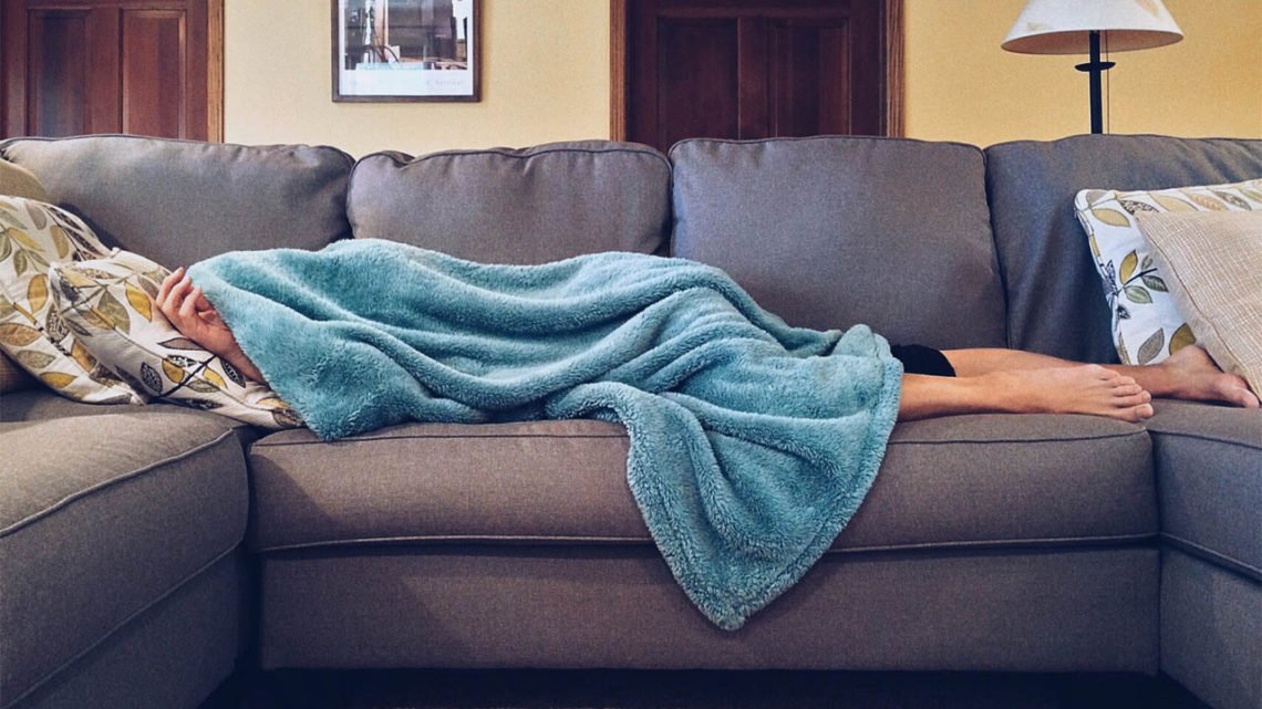 Mom lays on a gray couch, covered in a fuzzy blue blanket.