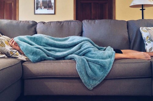 Mom lays on a gray couch, covered in a fuzzy blue blanket.