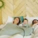 two parents laying in bed, napping with their toddler. The Connection Between Sleep and Emotional Well-Being for Parents